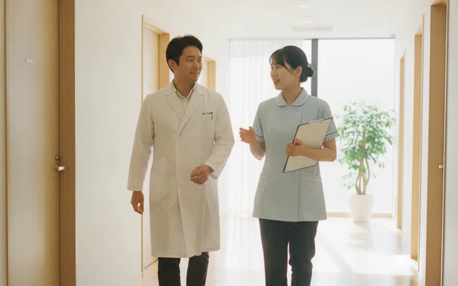 明るい院内の廊下で、話しながら並んで歩く医師と看護師(当社が運営する医療機関)
